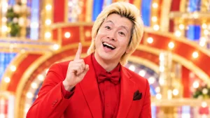 赤いスーツ姿で人差し指を上げる金髪男性のイメージ
