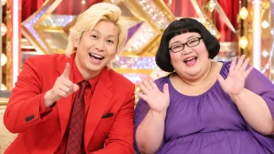 赤いスーツの金髪男性と紫色の衣装を着た女性のお笑いコンビのイメージ